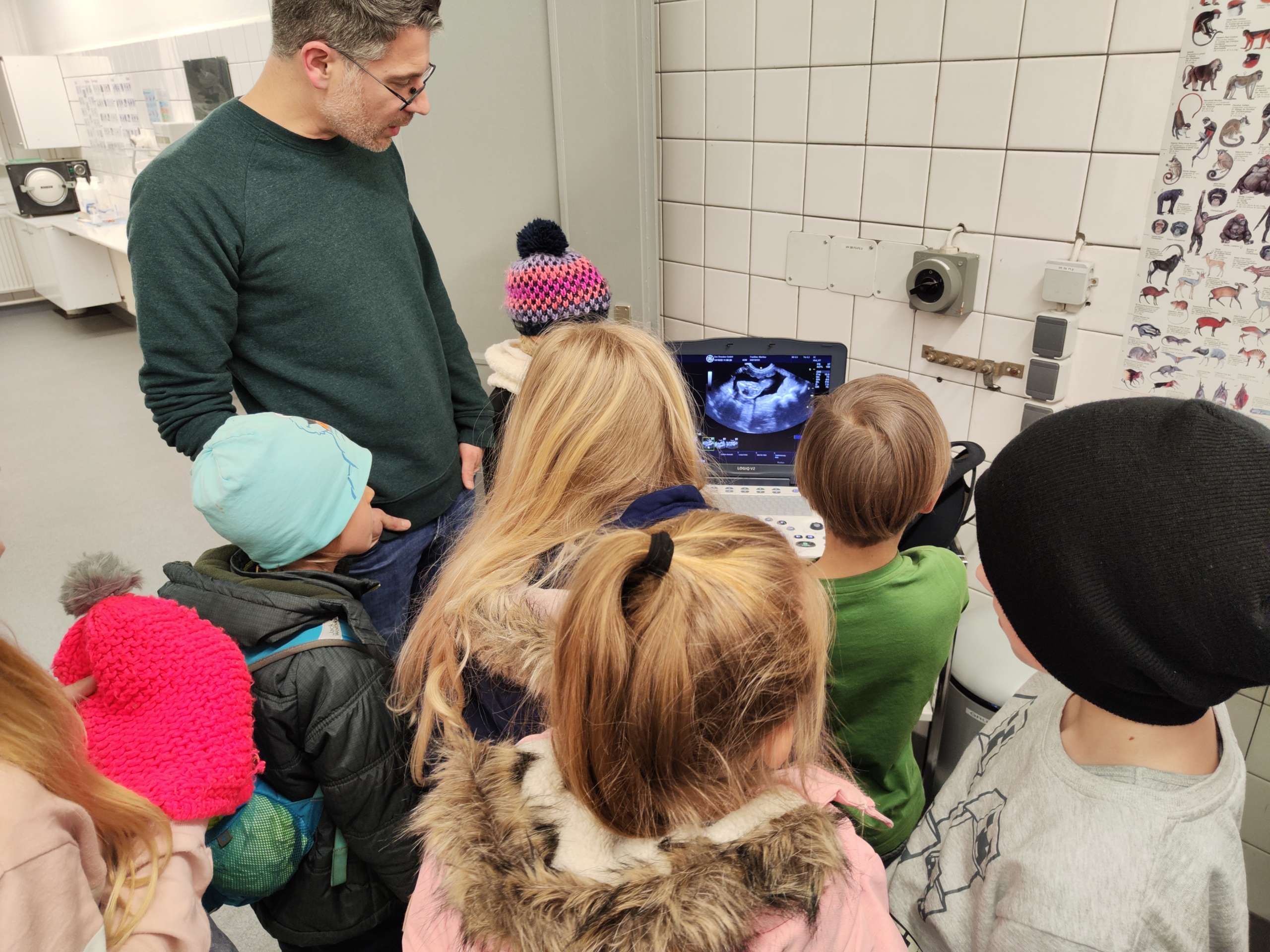 Kinder schauen mit einem Erwachsenen auf einen Ultraschall-Bildschirm in einem medizinischen Raum.