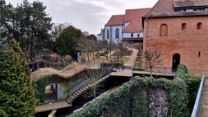 Mittelalterliche Klosteranlage mit rotem Sandsteinturm, Steganlage und winterlichem Garten, im Hintergrund gotische Kirche